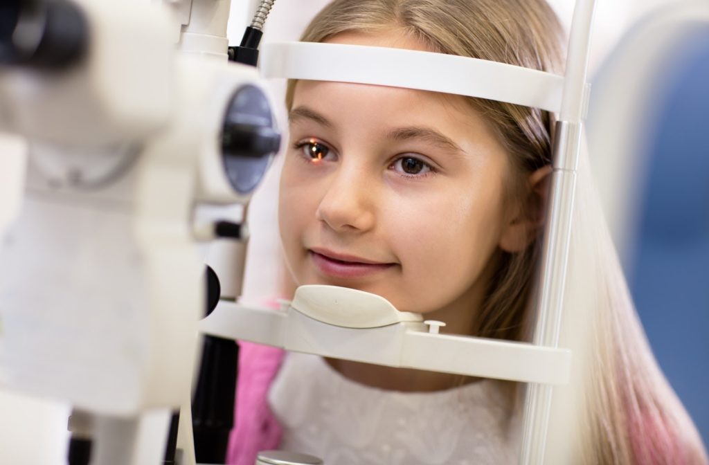 Girl undergoes eye exam with light flashed at her right eye at the optometrists office.