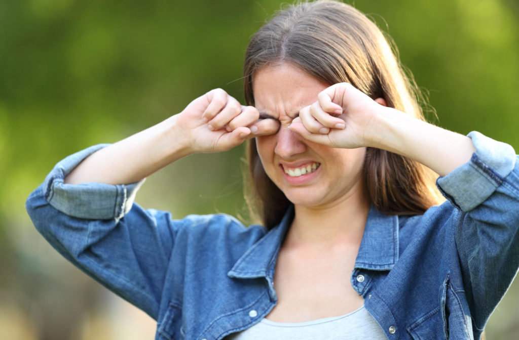 A young lady rubbing her irritated eyes with both hands outdoors