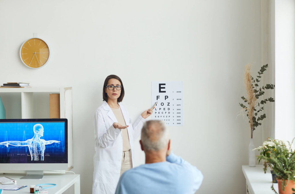 A female ophthalmologist pointing at an eye chart while testing the eyesight of a senior patient on his regular eye exam.