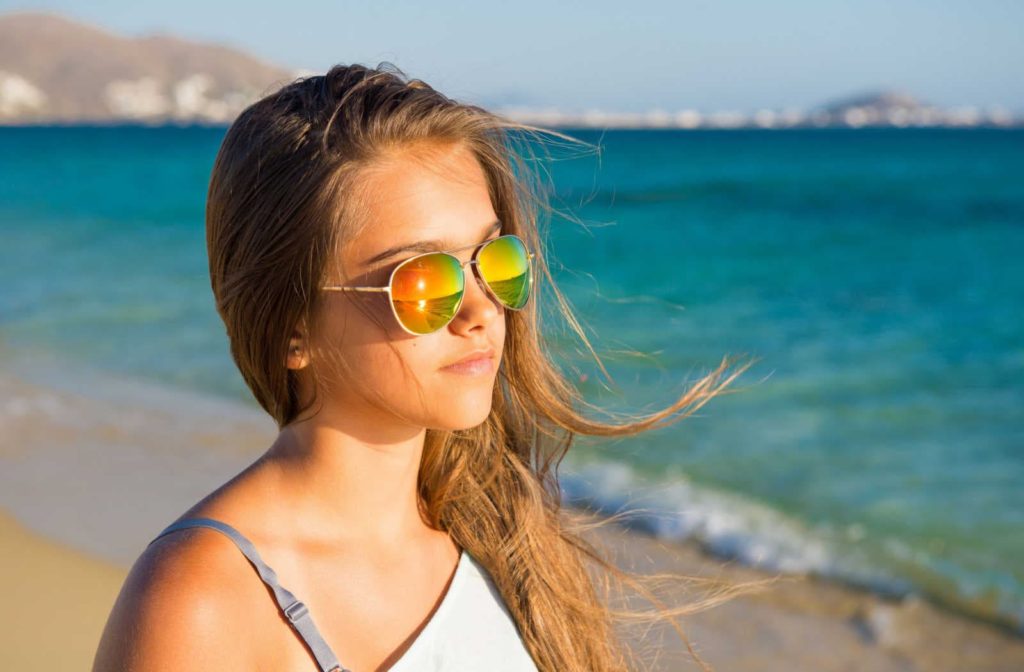 A young girl walking at the beach is wearing polarized sunglasses.