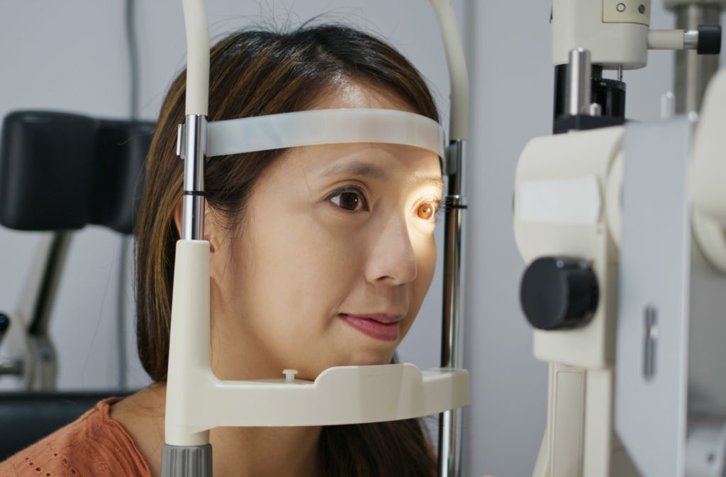 A woman resting her head on the chin rest of a medical apparatus used in eye exams.