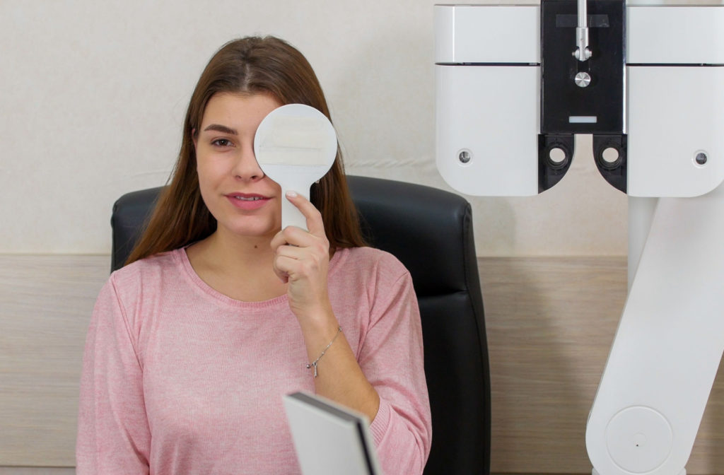 A woman undergoing a visual acuity test. She's also holding a white occluder to block her left eye.