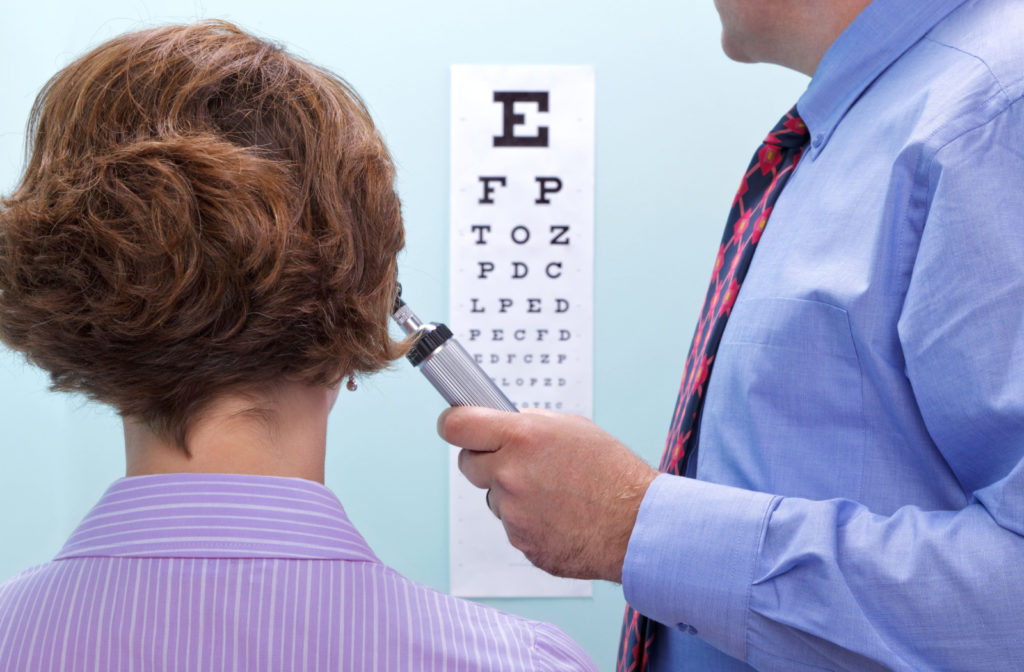 A woman undergoing a visual acuity test conducted by an optometrist who is holding a metal occluder.