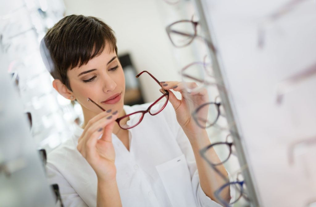 A young woman in a white shirt in a optic store holding eyeglasses frames in both hands before trying them on.